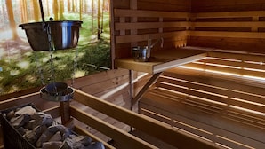 A sauna with wooden walls and a bench. There is a hanging pot and a bucket on the bench. - Kleindienst (Ursensollen)