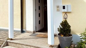 The entrance to Hotel Garni Kleindienst with a sign above the door, a potted plant, and a small outdoor area with steps leading up to the entrance. - Kleindienst (Ursensollen)