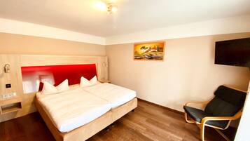 A modern hotel room with a large bed, a wooden headboard, a bedside table, a chair, and a painting on the wall.