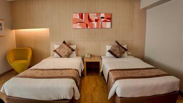 A hotel room with two beds, a bedside table with a phone, a lamp, and a yellow armchair.