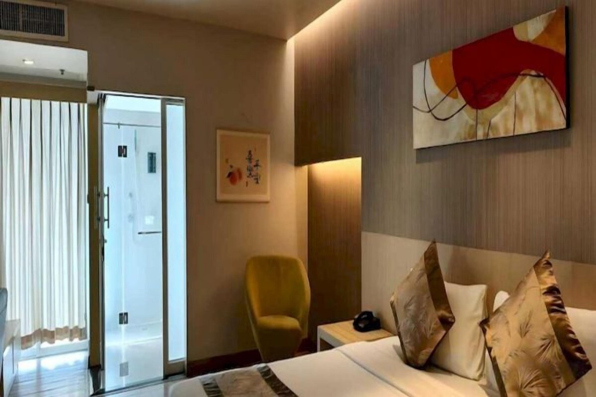 Habitación de hotel con una cama, una silla, una mesita de noche y una puerta que da a un balcón.