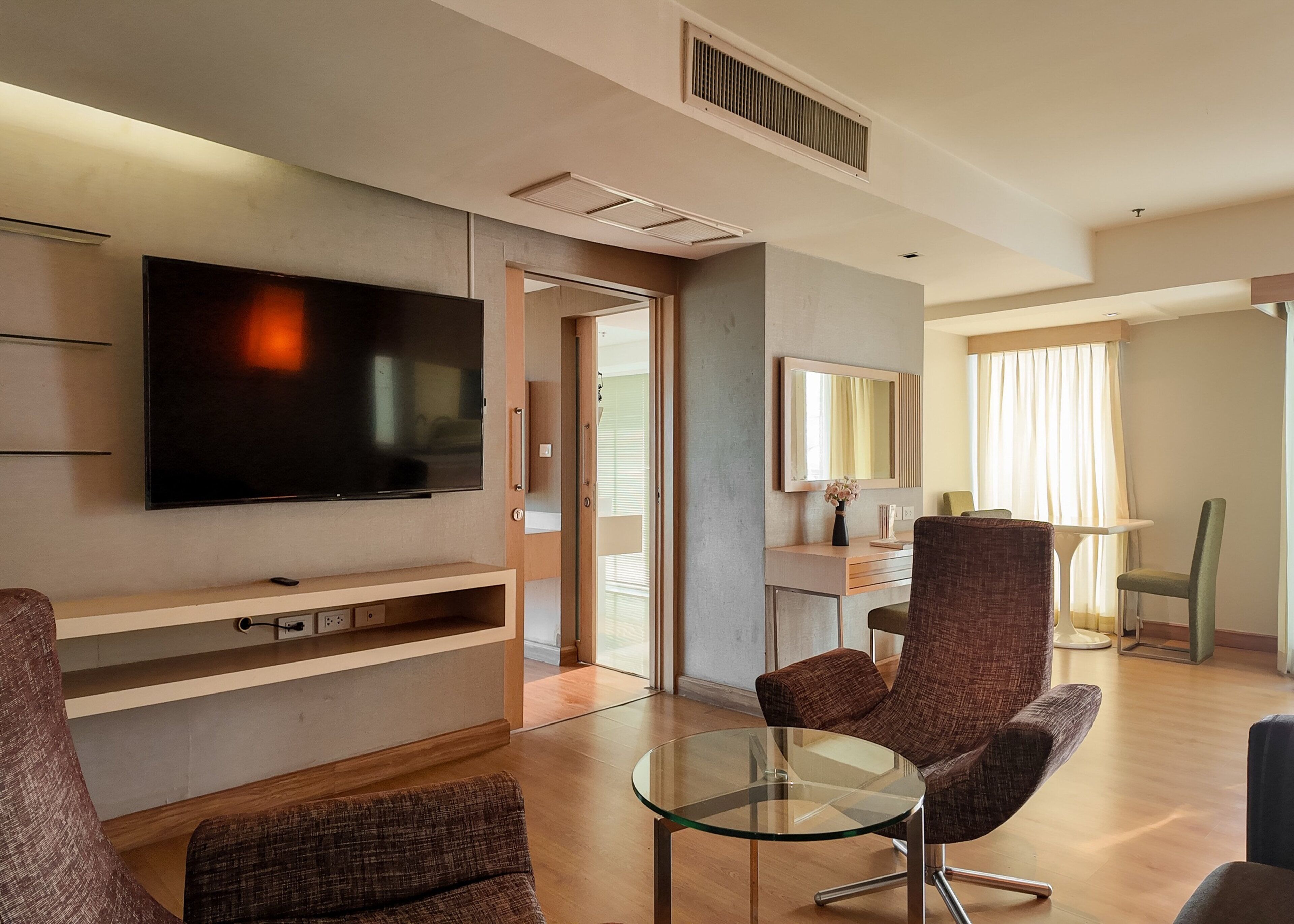 A modern living room with a flat-screen TV, a glass coffee table, and two brown armchairs.