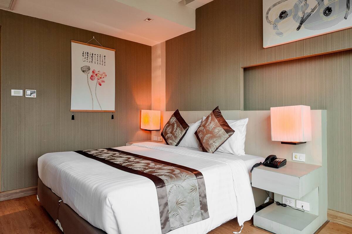 A hotel room with a large bed, bedside lamps, a nightstand, a wall-mounted telephone, and a painting.