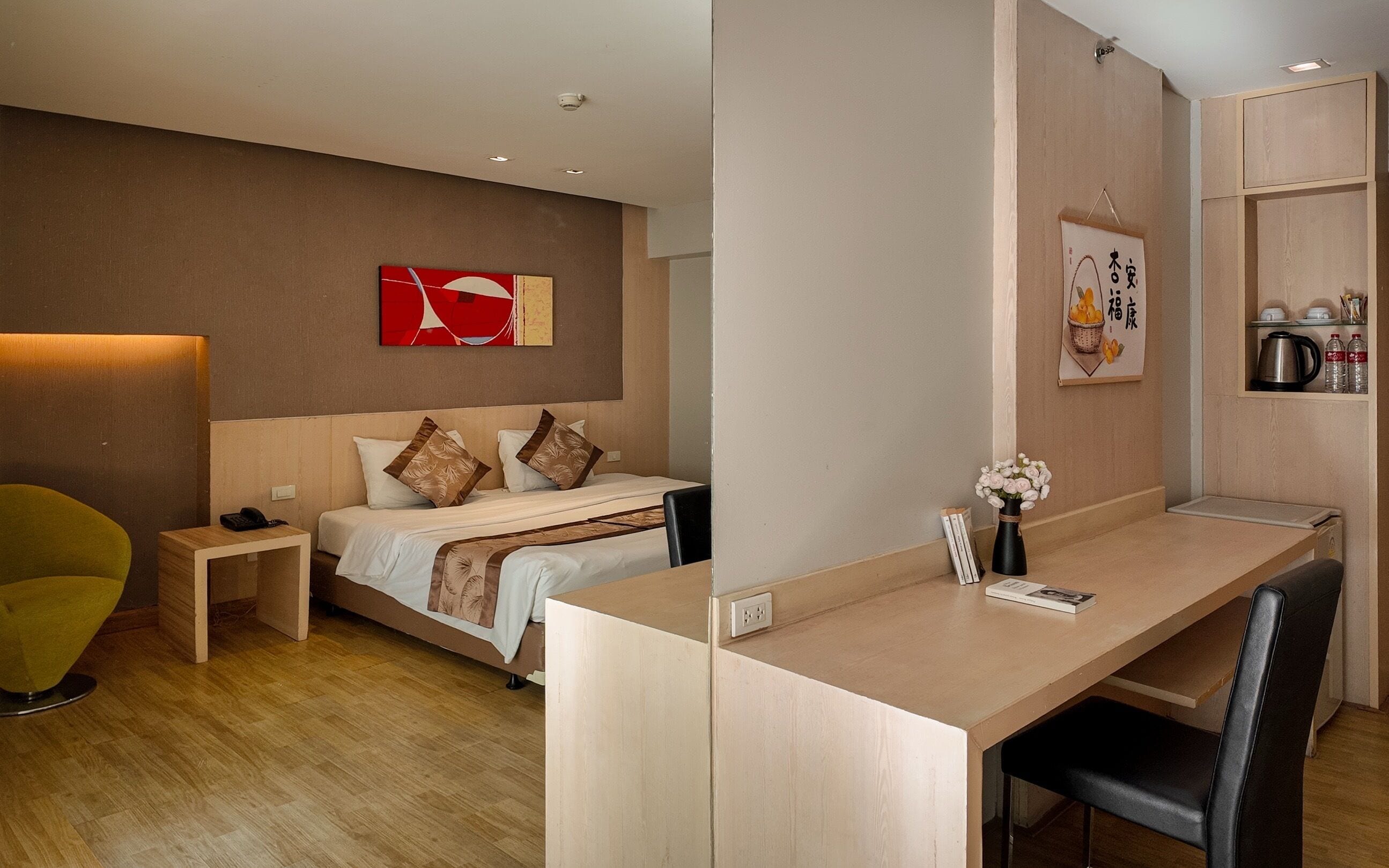A hotel room with a bed, bedside table, desk, chair, and a wall with artwork.