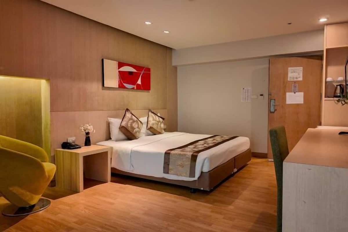 A hotel room with a bed, bedside table, chair, and a desk with a chair.