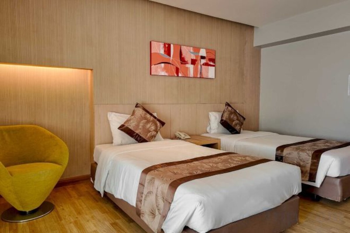 Habitación de hotel con dos camas, una mesita de noche, una silla y una obra de arte colgada en la pared.