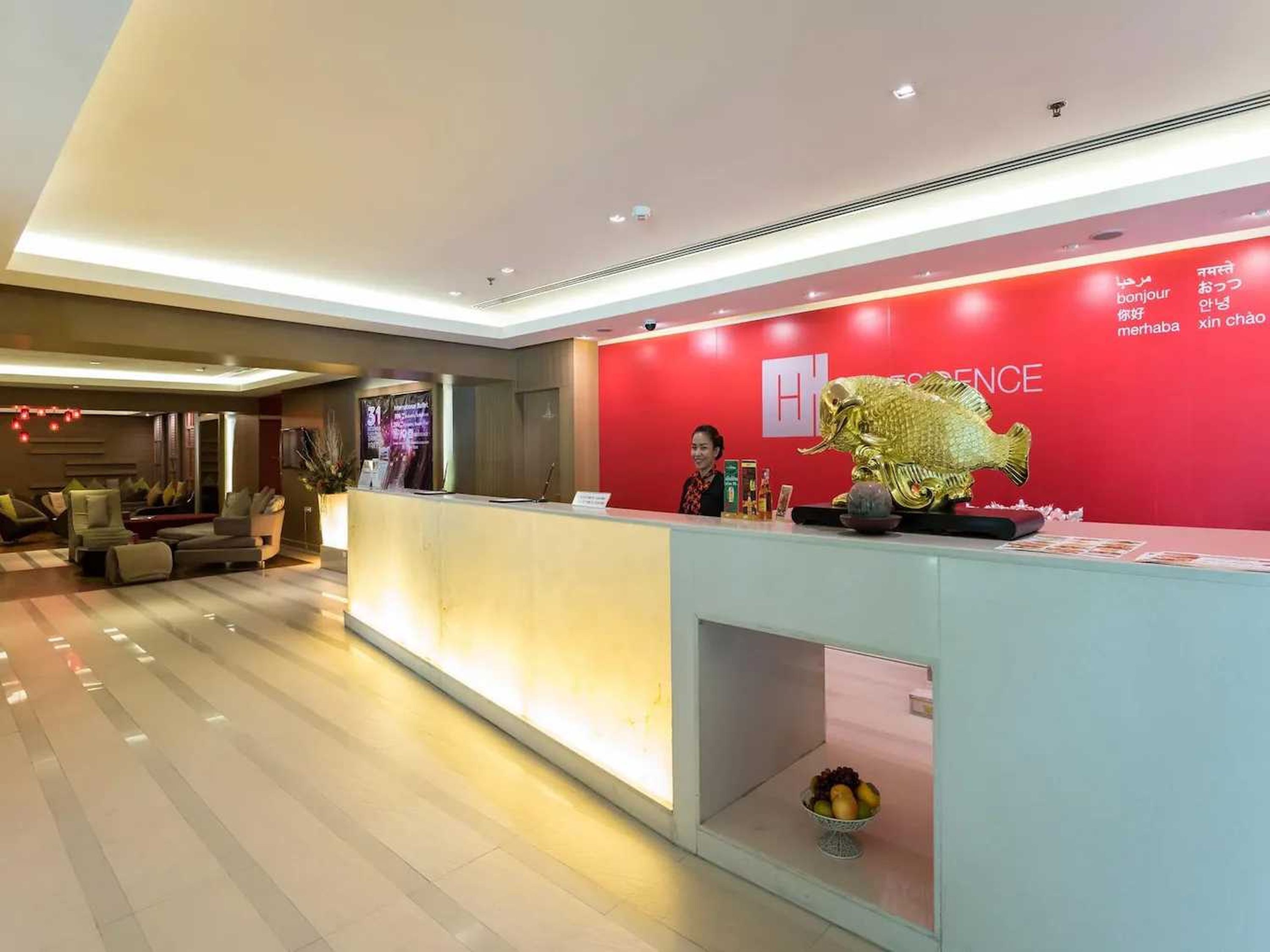 Zona de recepción de un hotel con una pared roja, una recepcionista y una estatua de un pez dorado.