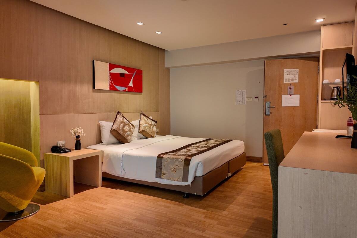 A modern hotel room with a bed, bedside table, chair, and a painting on the wall.