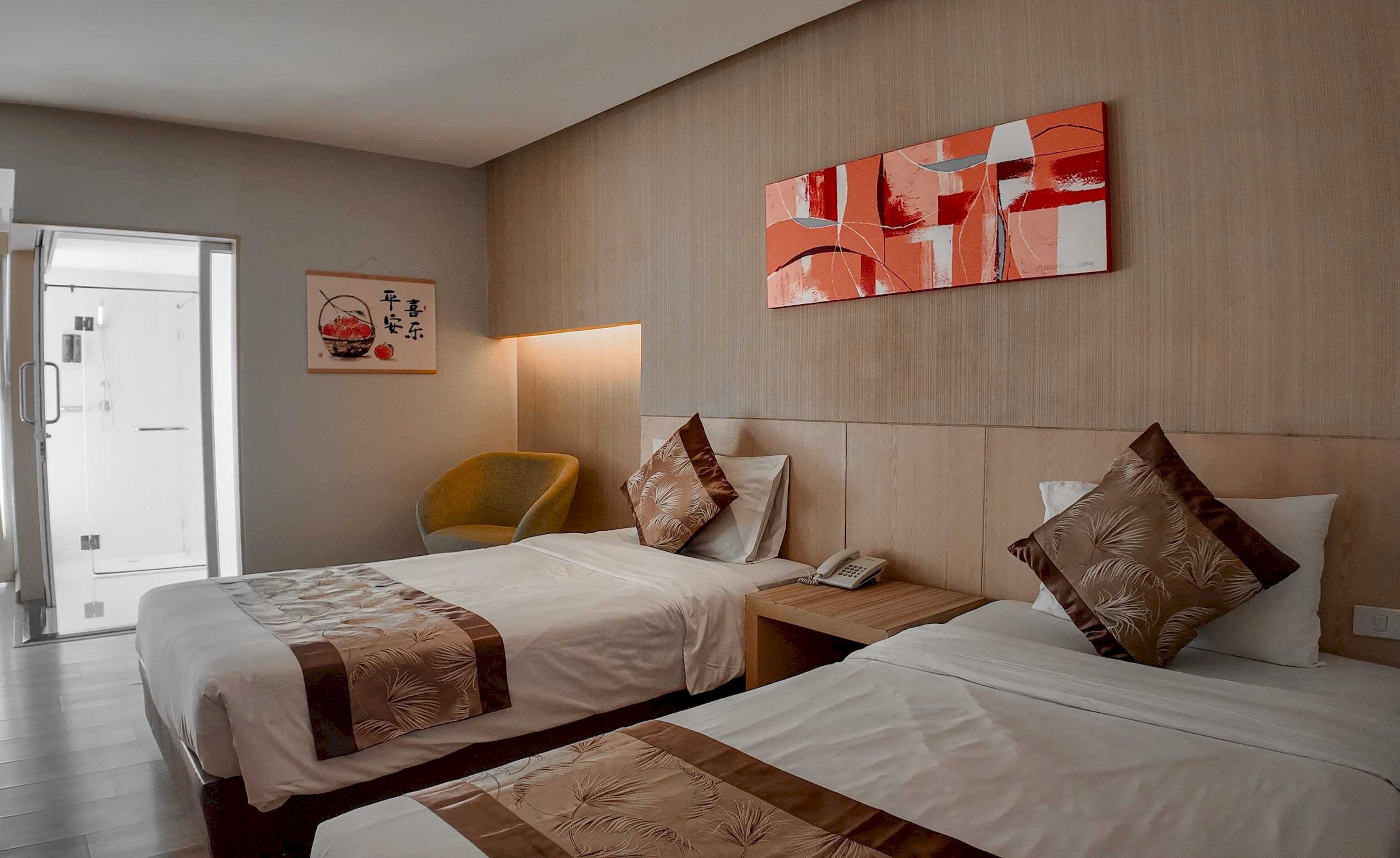 A hotel room with two beds, a chair, a bedside table with a phone, and artwork on the wall.