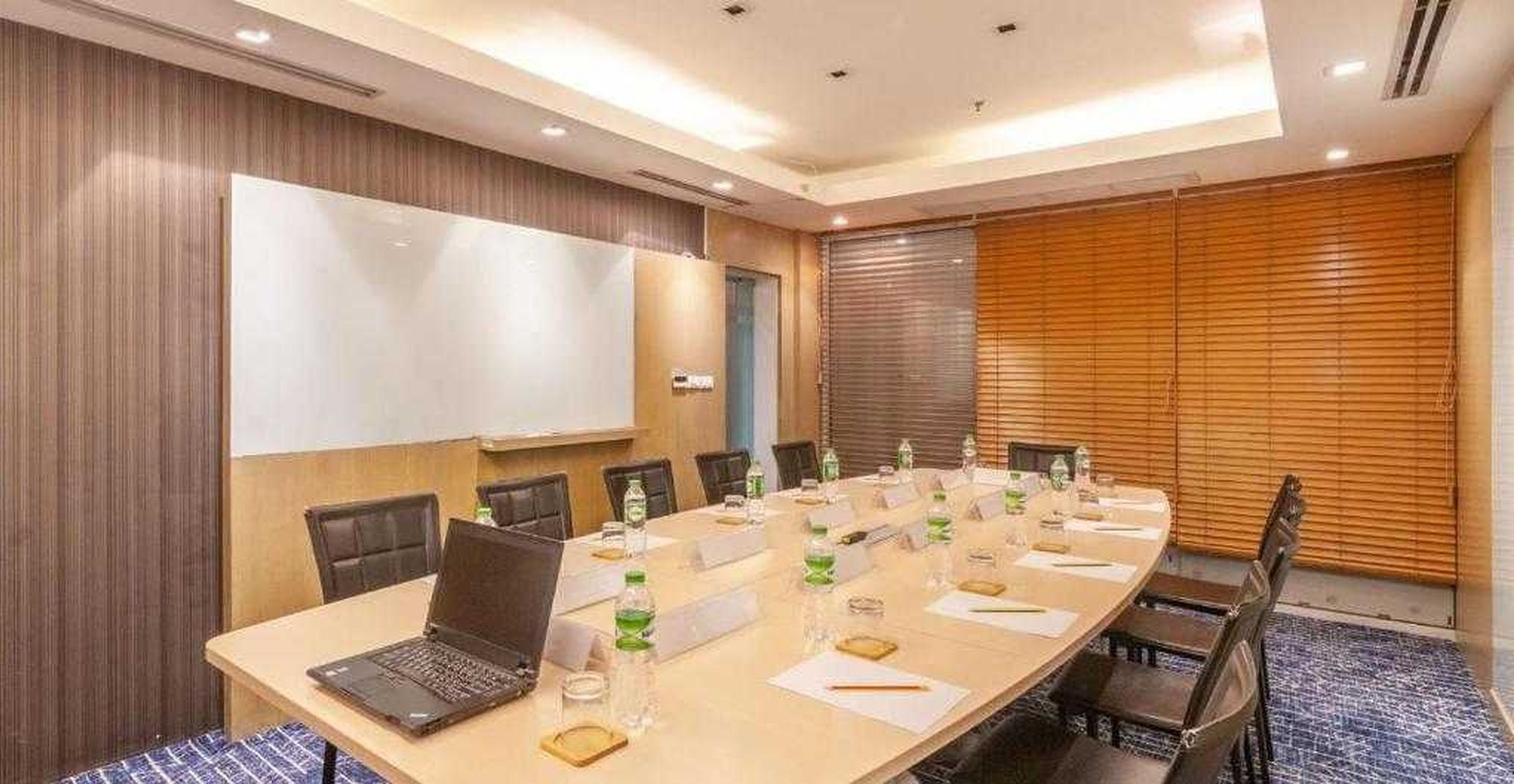 A conference room with a long table, chairs, a laptop, nameplates, water bottles, and a whiteboard.