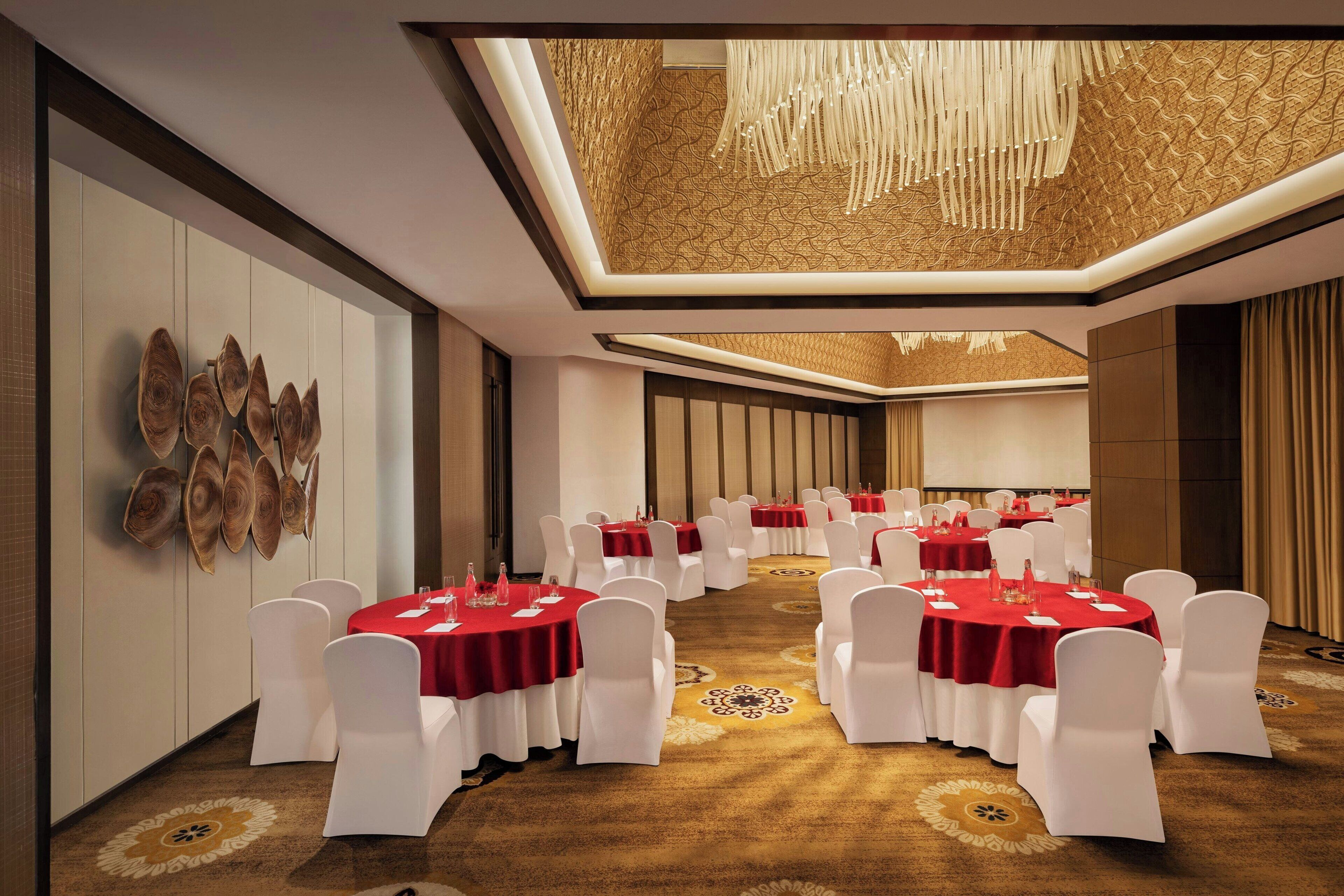 A conference room with round tables, white chairs, and red tablecloths.