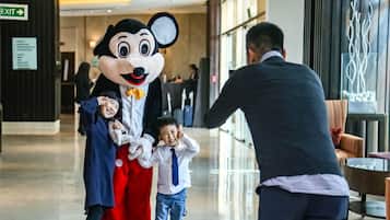 A person in a Mickey Mouse costume interacting with two children in a hotel lobby.