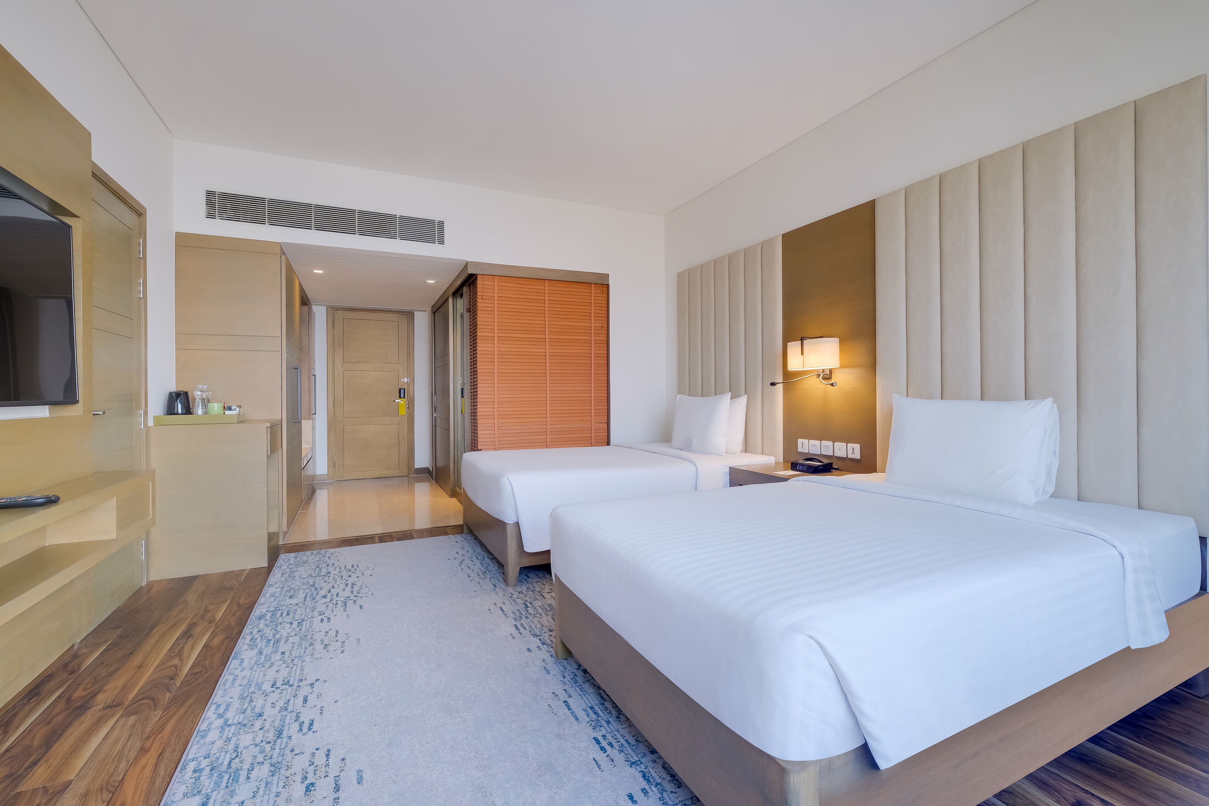 A hotel room with two beds, a TV, a desk, and a bathroom.