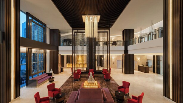 A spacious lobby with a central seating area, a chandelier, and a view of the cityscape through large windows. - Courtyard by Marriott Gurugram Downtown (Gurugram)