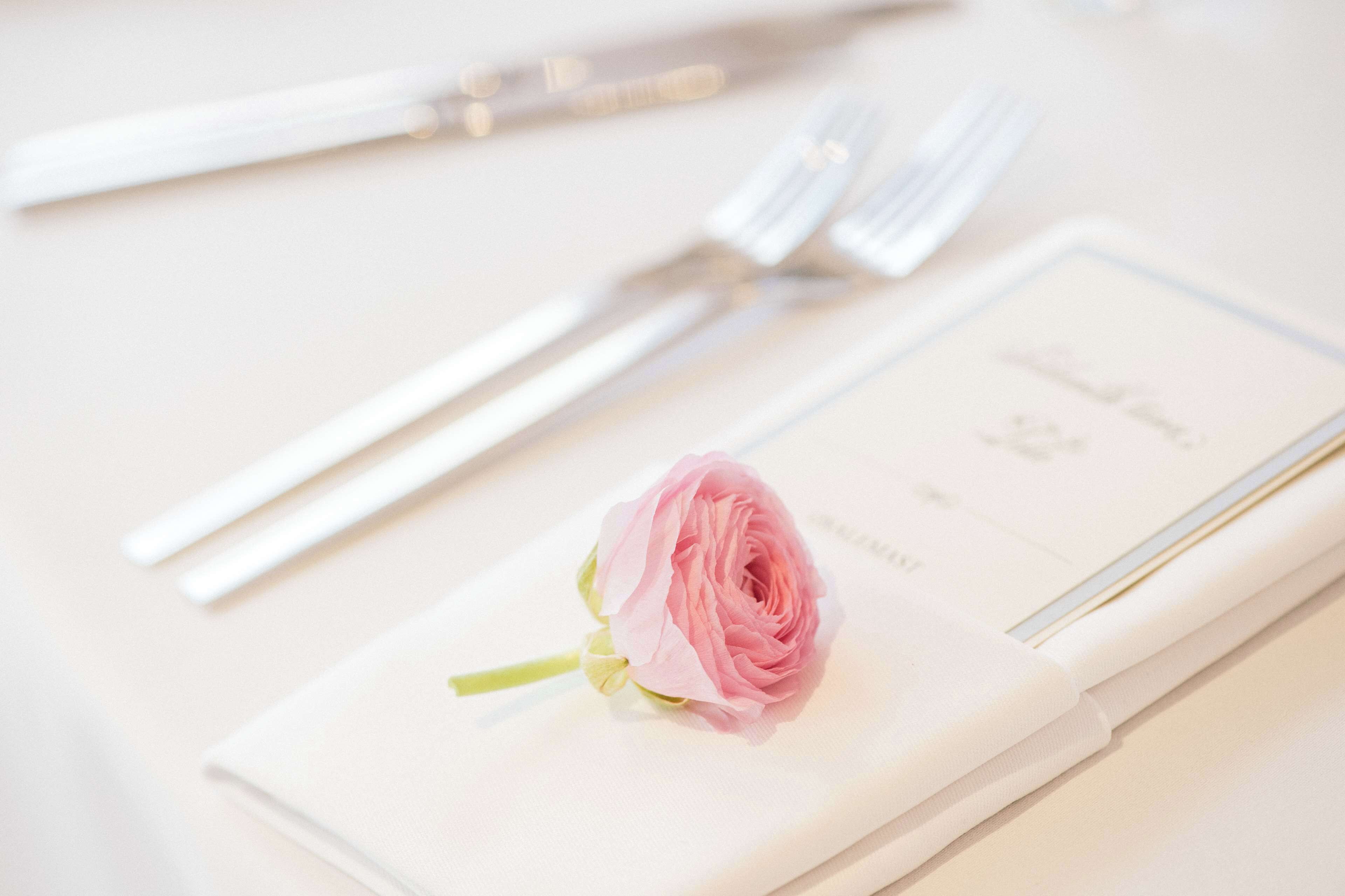 Une table élégamment dressée, avec une serviette pliée, une rose rose et des couverts en argent.