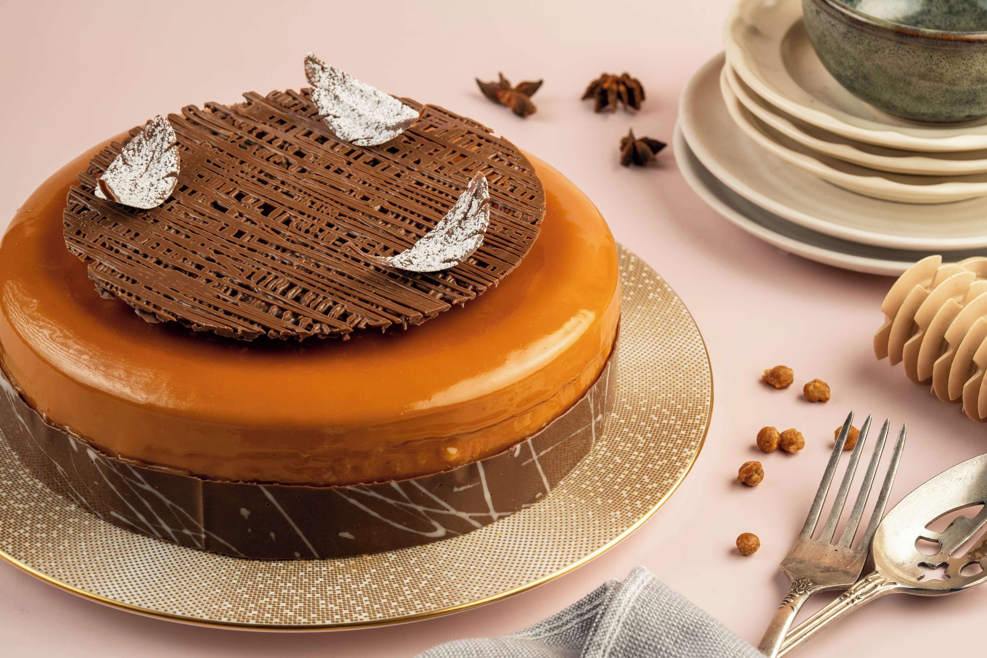 A round cake with a chocolate lattice top and decorative silver leaves, placed on a gold-rimmed cake stand.