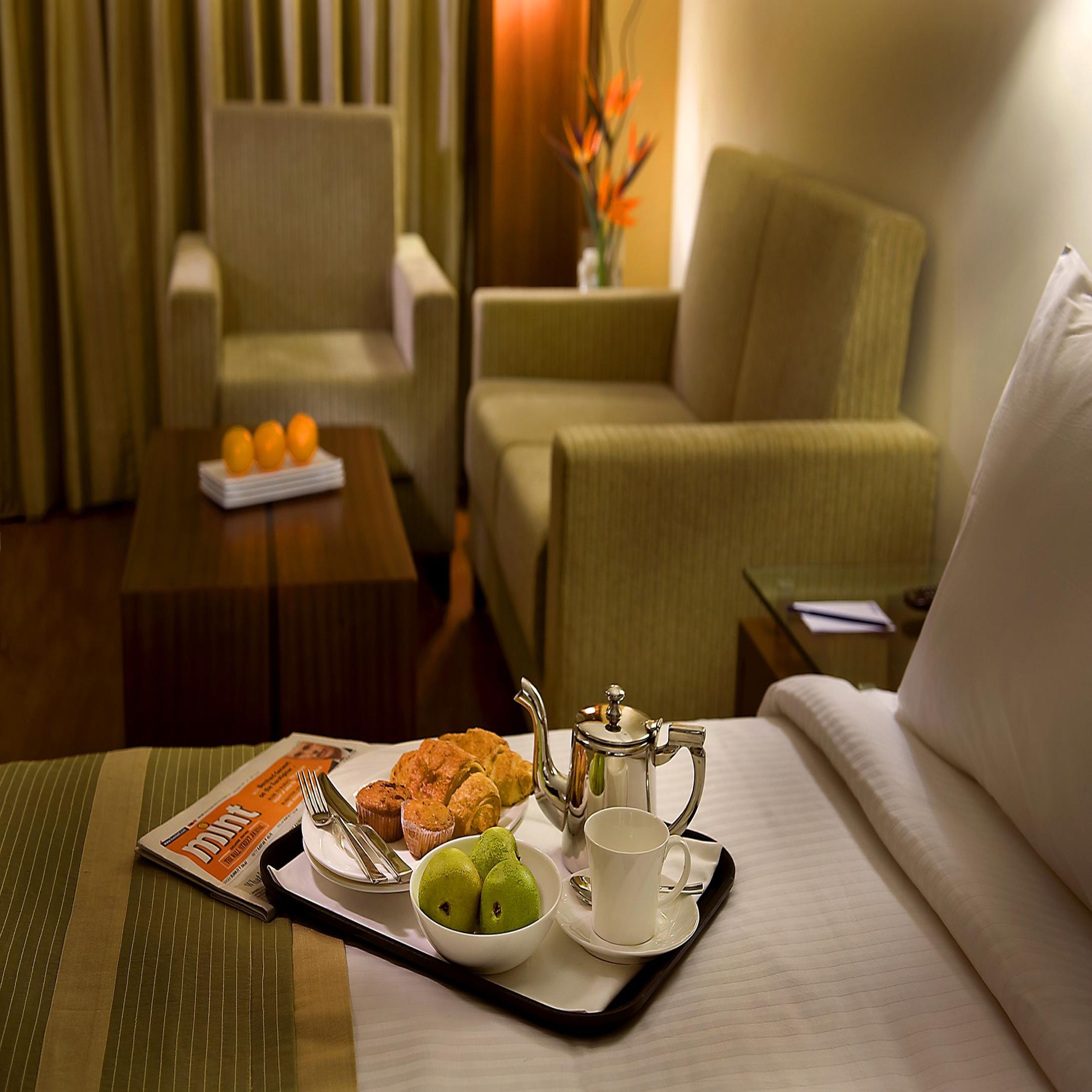 Ein Hotelzimmer mit einem Bett, einem Couchtisch mit Orangen, einer Ablage mit Gebäck, einem Teekessel und einer Obstschale.