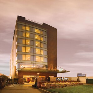 A multi-story hotel with a glass facade, a visible entrance, and a sign indicating a lounge bar. - Park Inn, Gurgaon (Gurugram)
