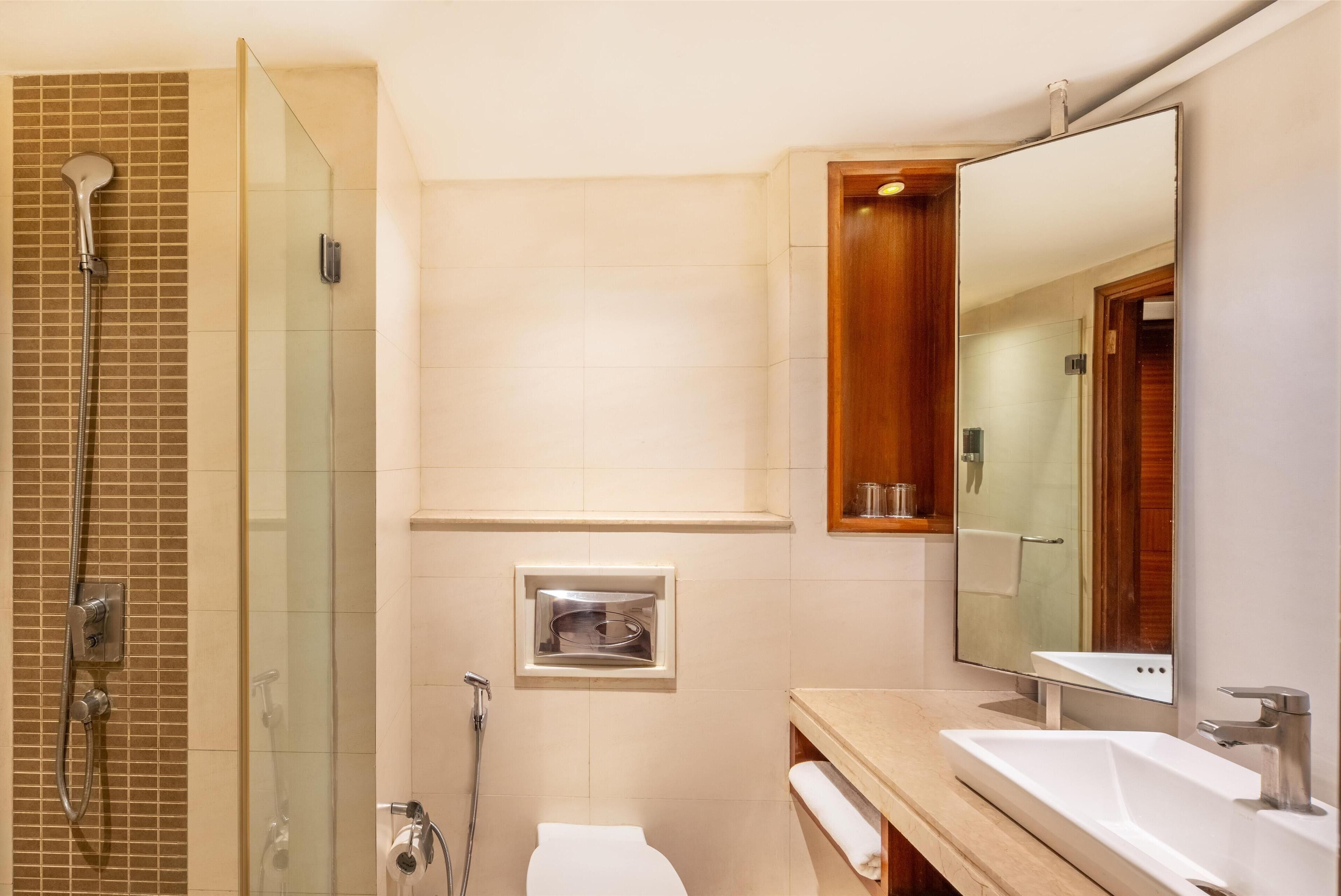 Un baño moderno con ducha envuelta en vidrio, inodoro, lavamanos y un espejo grande.