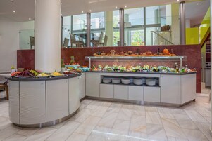 Buffet com diversas frutas e bebidas, piso de mármore e design de interiores moderno.