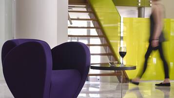 Una silla morada con forma de corazón, una mesita con una copa de vino, y una escalera al fondo.