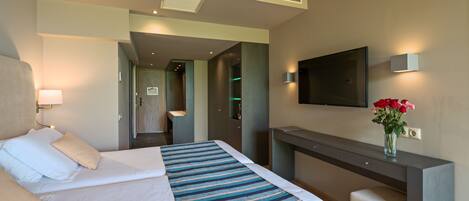 Una habitación de hotel con cama, escritorio, televisor y un florero con flores.