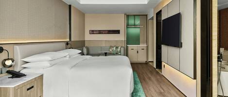 A modern hotel room with a large bed, a desk, a flat-screen TV, and a green patterned rug.