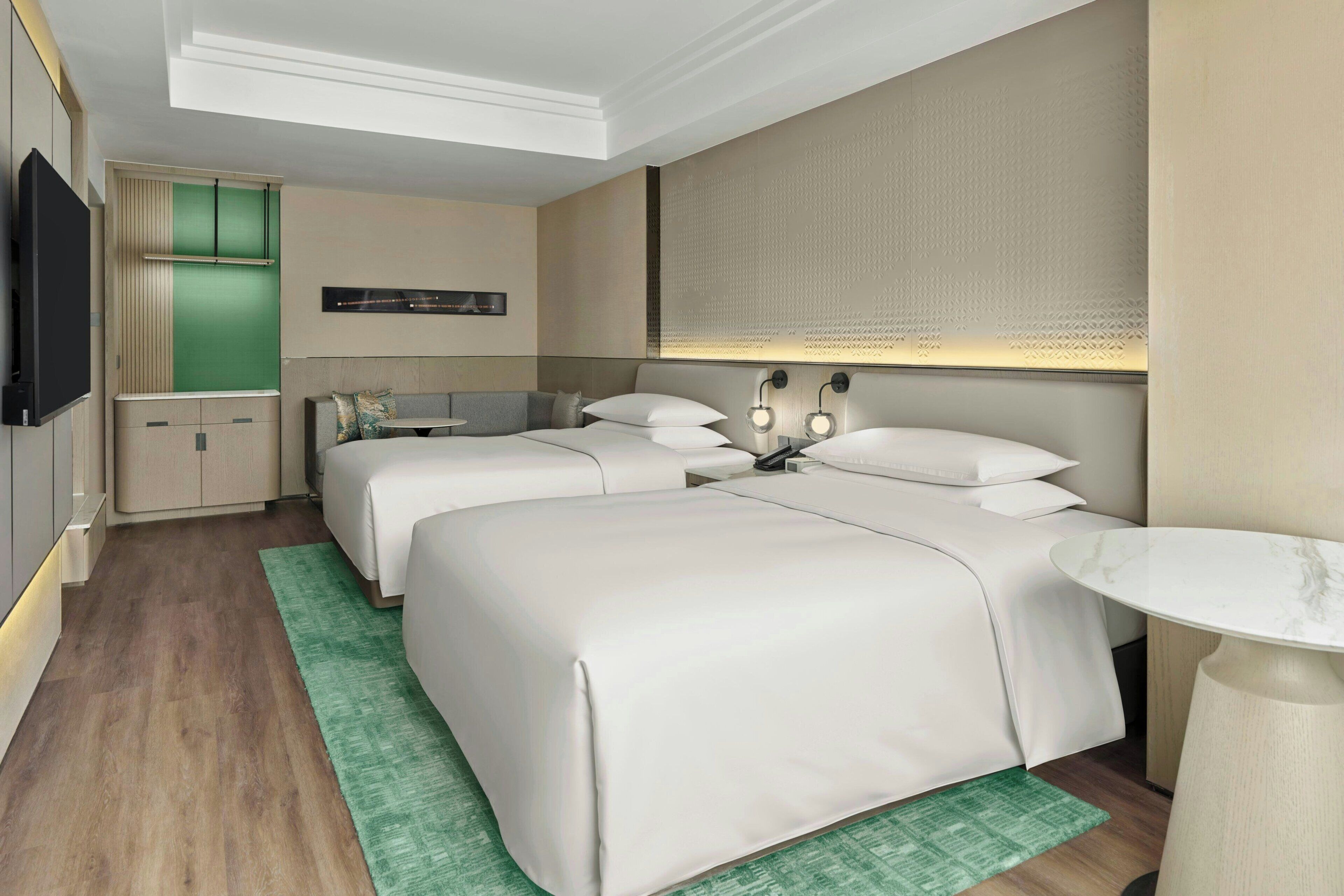 A hotel room with two beds, a small desk, a television, and a green rug.