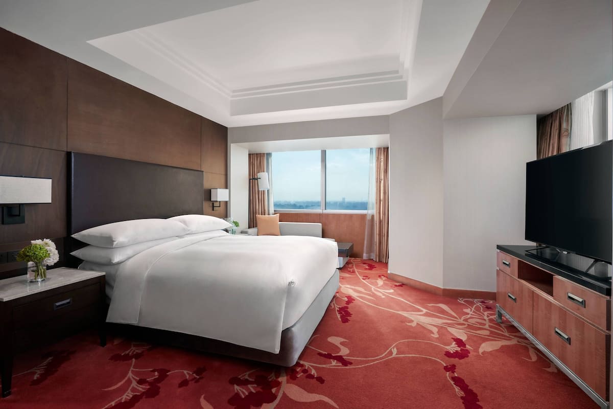 A hotel room with a large bed, a TV, a nightstand, a dresser, and a window with a city view.