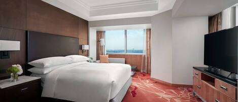 Habitación de hotel con una cama grande, televisor, mesita de noche, cómoda y ventana con vista a la ciudad.
