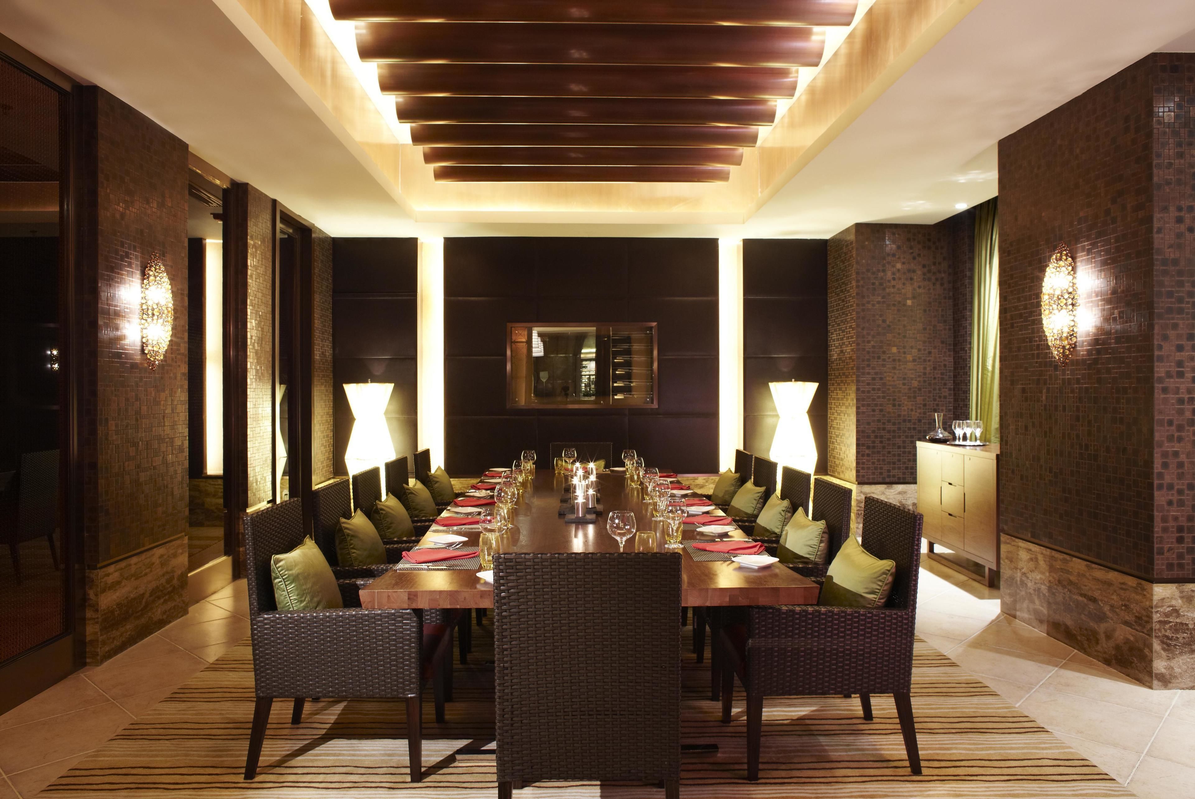 Une salle à manger élégante, avec une longue table dressée pour un repas, entourée de chaises en osier et éclairée par des appliques murales.