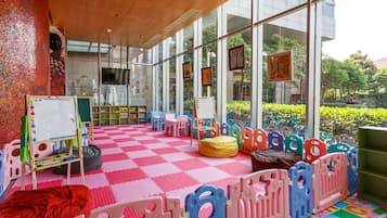 A brightly lit indoor play area with a checkered floor, colorful play structures, and a whiteboard.