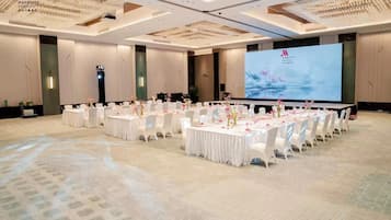 A large, well-lit conference room with multiple round tables, each set with white tablecloths and pink flowers.