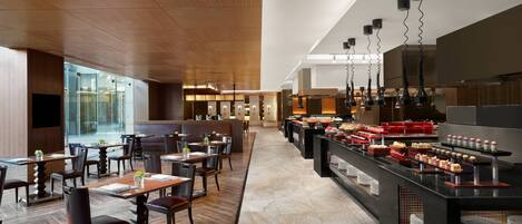 A modern restaurant with wooden flooring, a buffet area, and a seating area with tables and chairs.