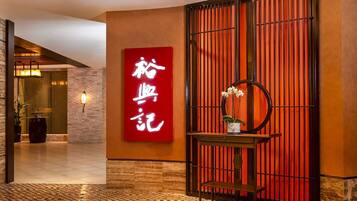 A hotel lobby with a tiled floor, a red sign with white text, a wooden bench, and a wall with vertical slats.
