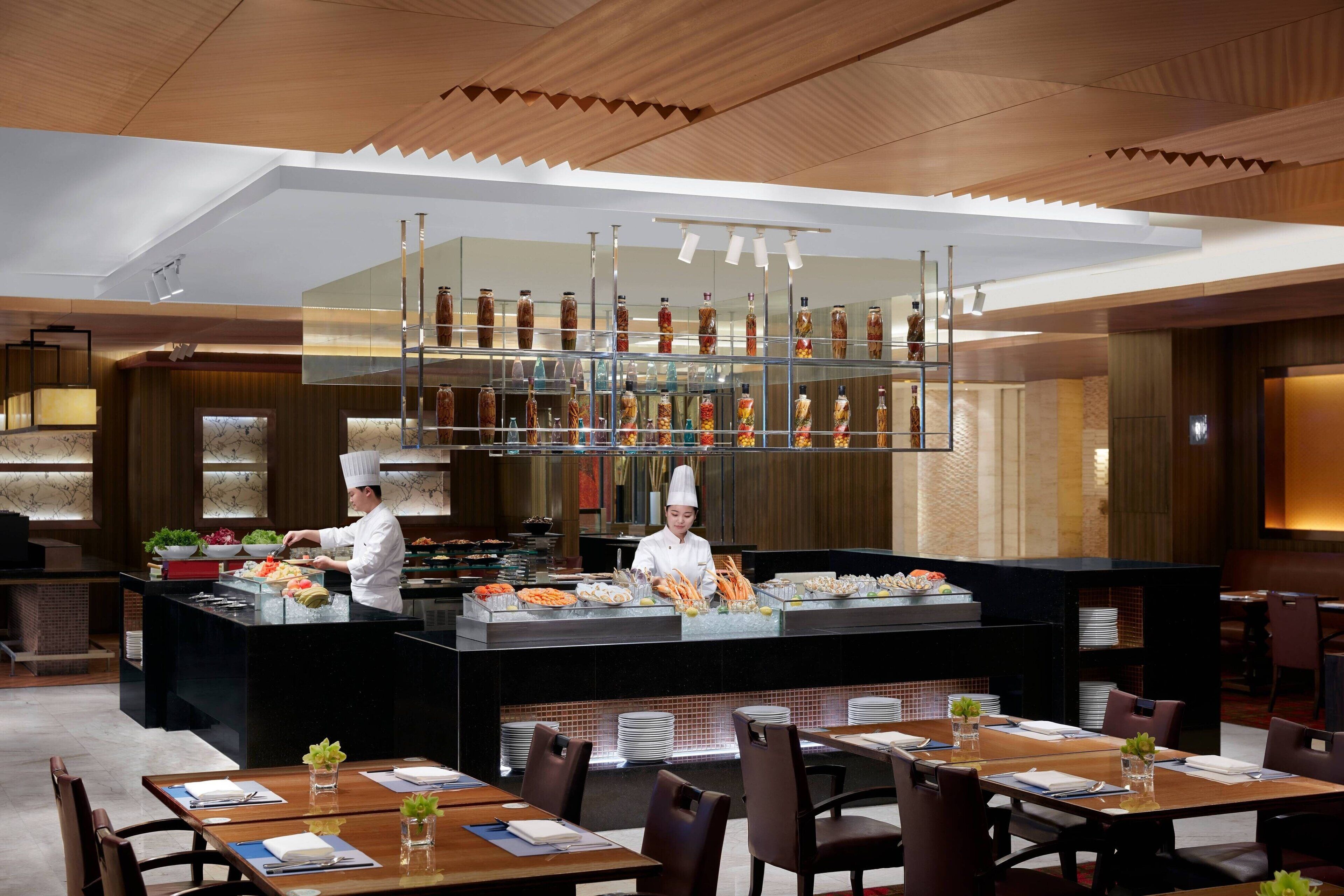 Een modern restaurant met een centraal bargedeelte, diverse zitmogelijkheden en een kok die aan het koken is.
