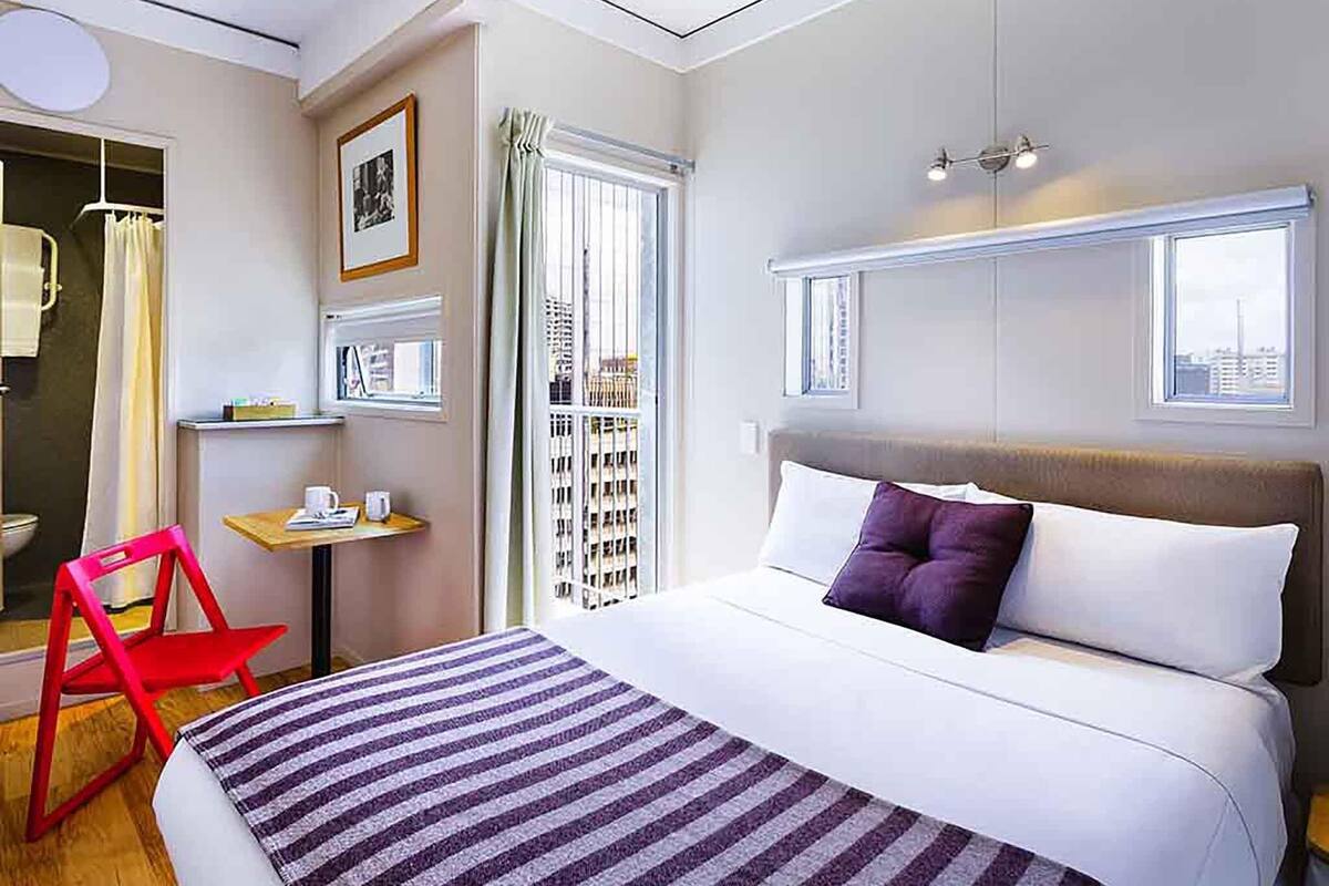 A hotel room with a bed, a desk, a chair, and a window with a city view.