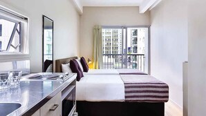 Una moderna camera d'albergo con un letto, un angolo cottura e un balcone con vista sulla città.
