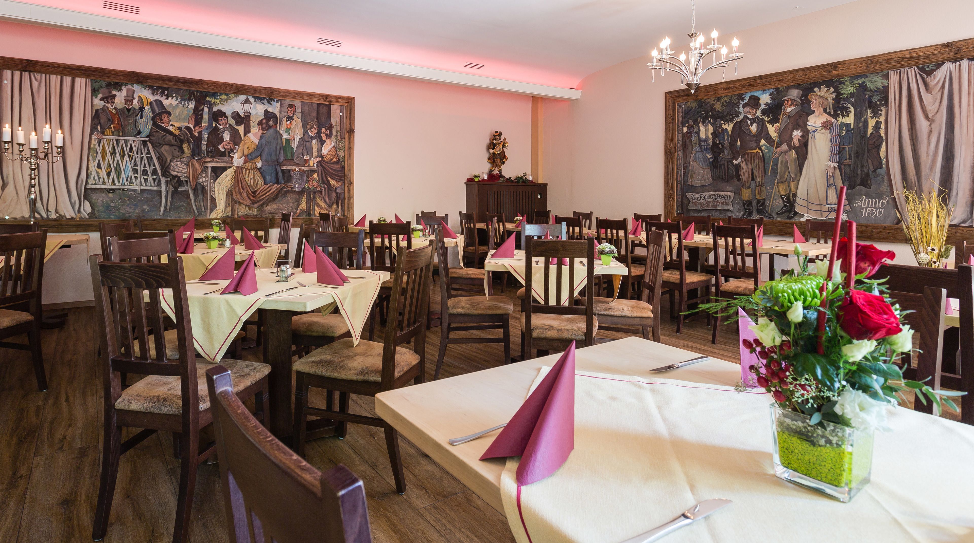 A restaurant with wooden tables and chairs, paintings on the walls, and a chandelier.