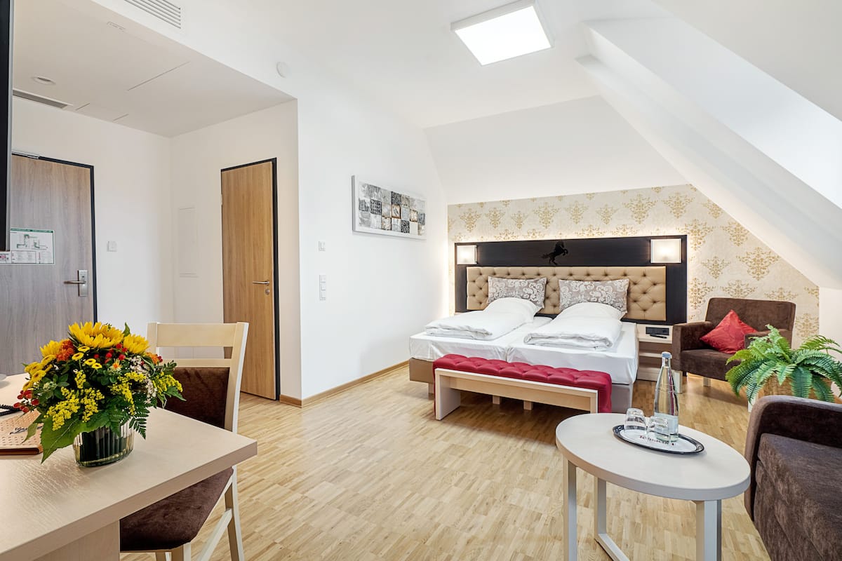 Ein modernes Hotelzimmer mit Bett, Schreibtisch, Stuhl, kleinem Tisch und einer Topfpflanze.