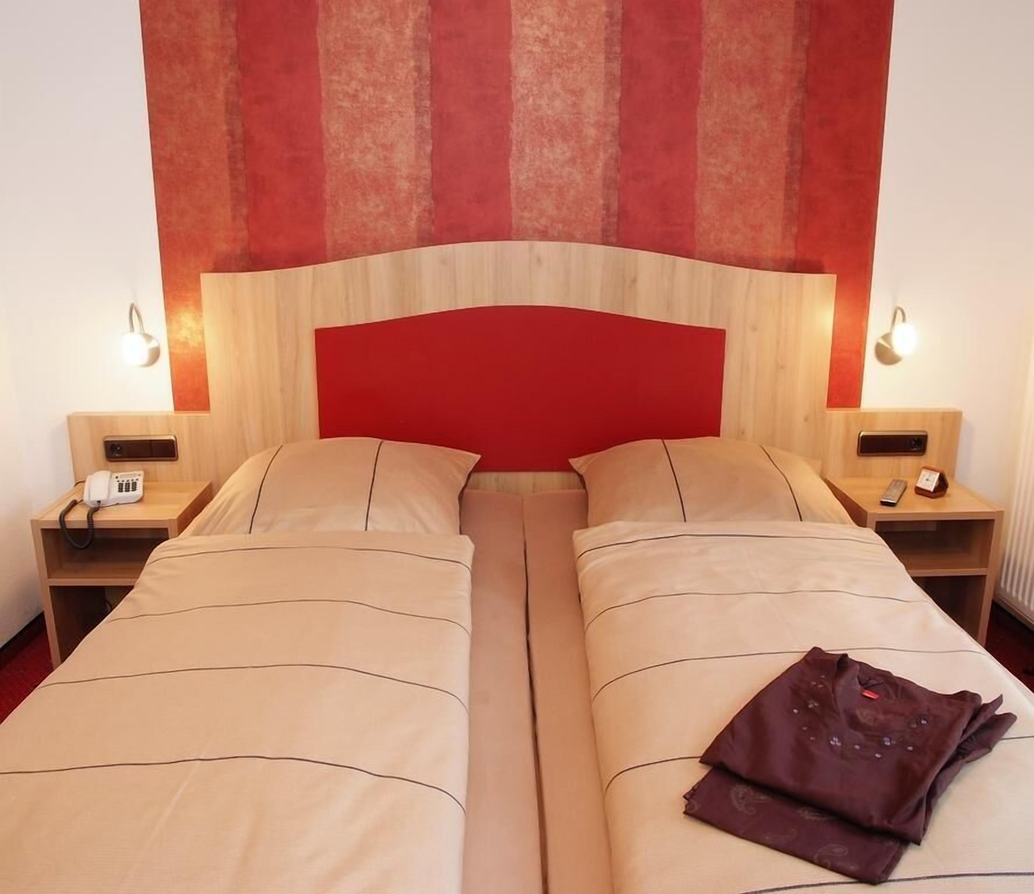 A double bed with a red headboard, two bedside tables with lamps, and a brown jacket on the bed.