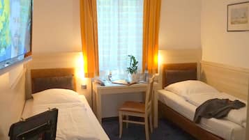 A hotel room with two single beds, a desk with a chair, a TV, and a suitcase on the floor.