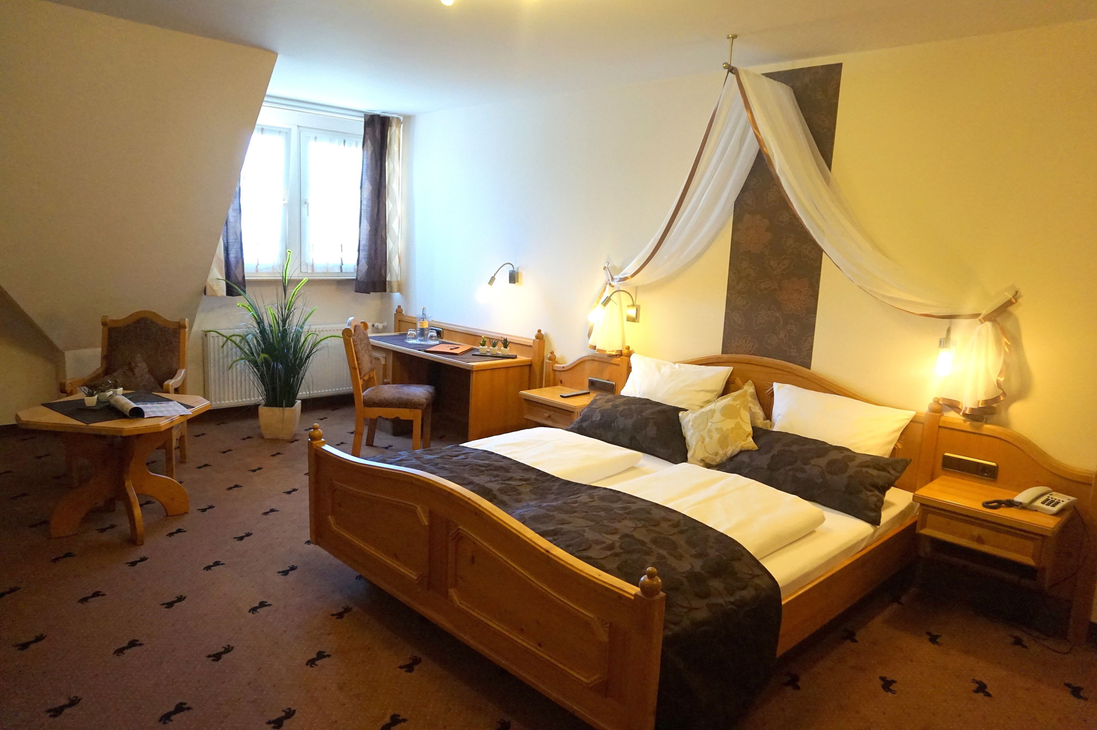 Une chambre d’hôtel avec un grand lit, un bureau, une chaise, une table de chevet et une plante en pot.