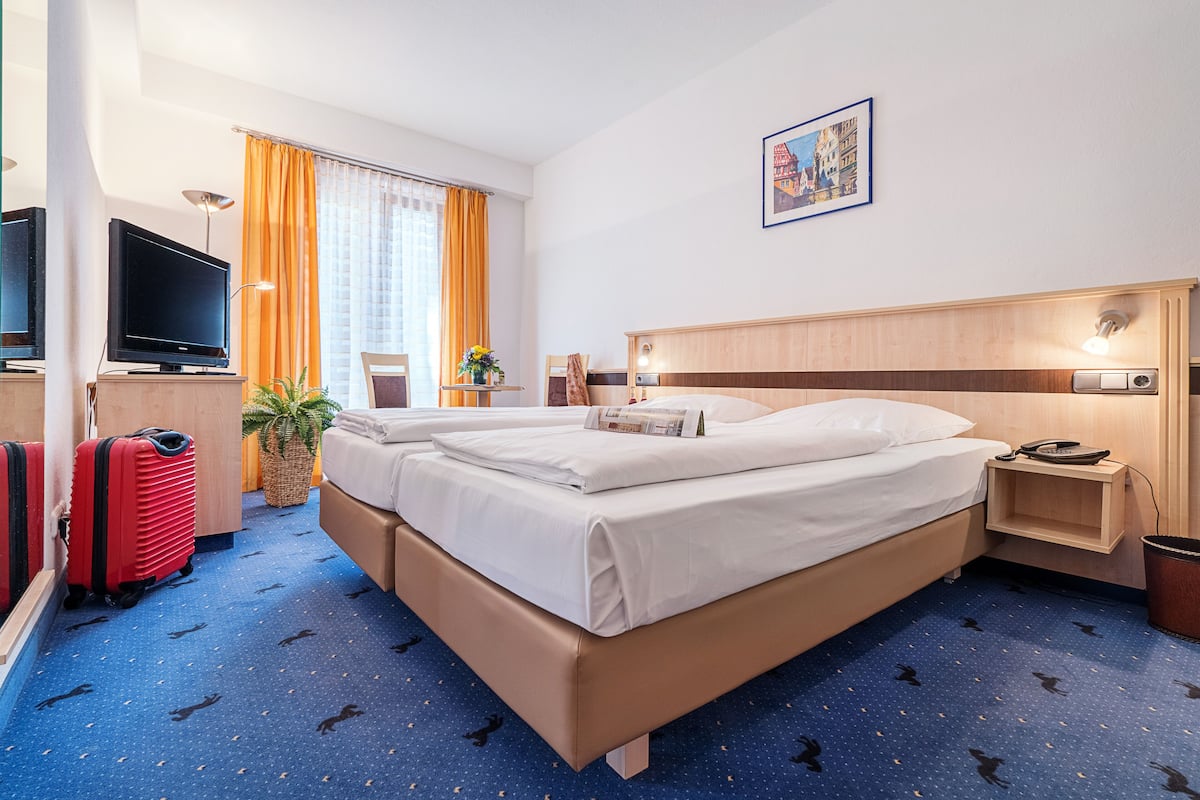 Ein Hotelzimmer mit Bett, Fernseher, Schreibtisch und einem Vorhangfenster.
