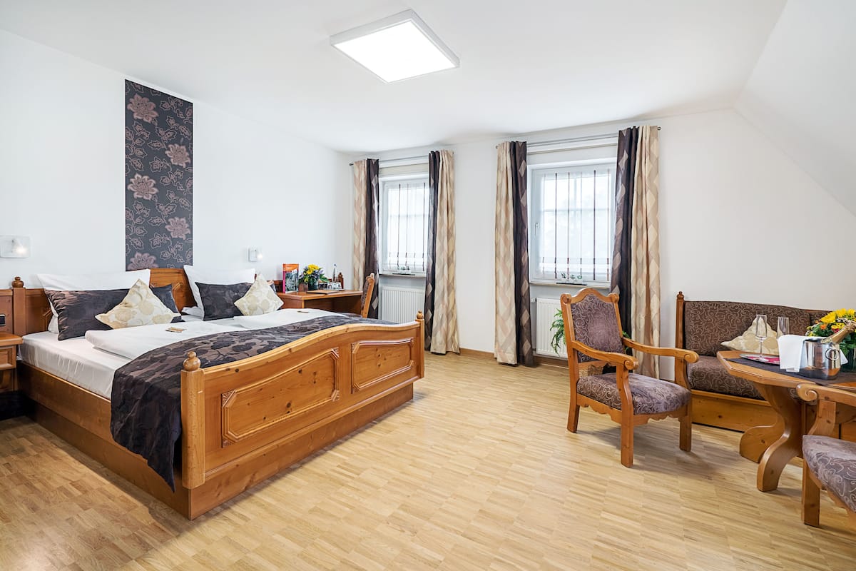 Ein Schlafzimmer mit einem hölzernen Bett, einem Holzstuhl, einem Holztisch und einem Fenster mit Vorhängen.
