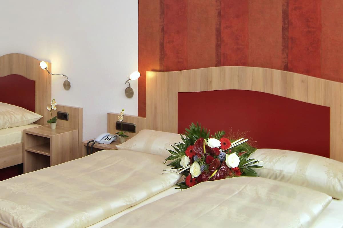 Ein Hotelzimmer mit zwei Einzelbetten, einem Nachttisch mit Lampe, einem Telefon und einer Blumenkomposition.