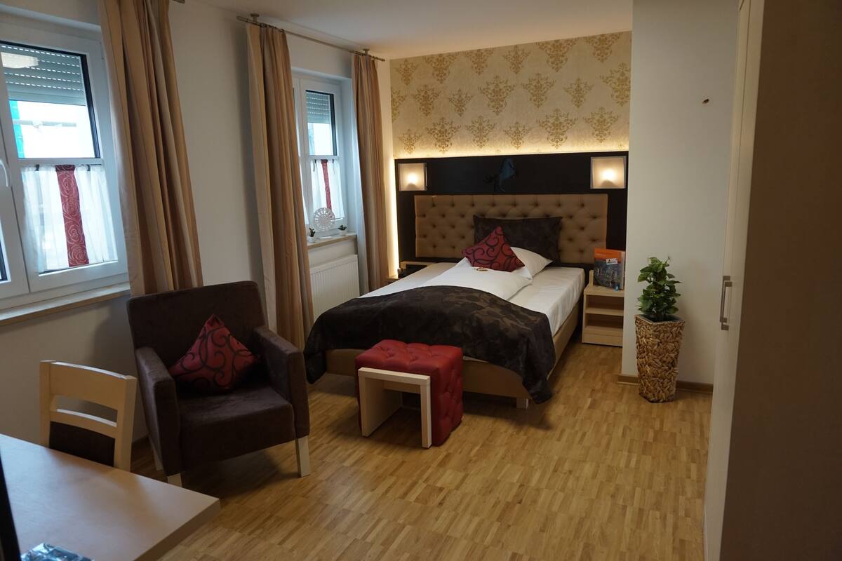 Ein Hotelzimmer mit einem Bett, einem Sessel, einem kleinen Tisch und einer Zimmerpflanze.