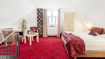 Une chambre d’hôtel avec un lit, un bureau, une chaise, une plante et une fenêtre avec des rideaux.