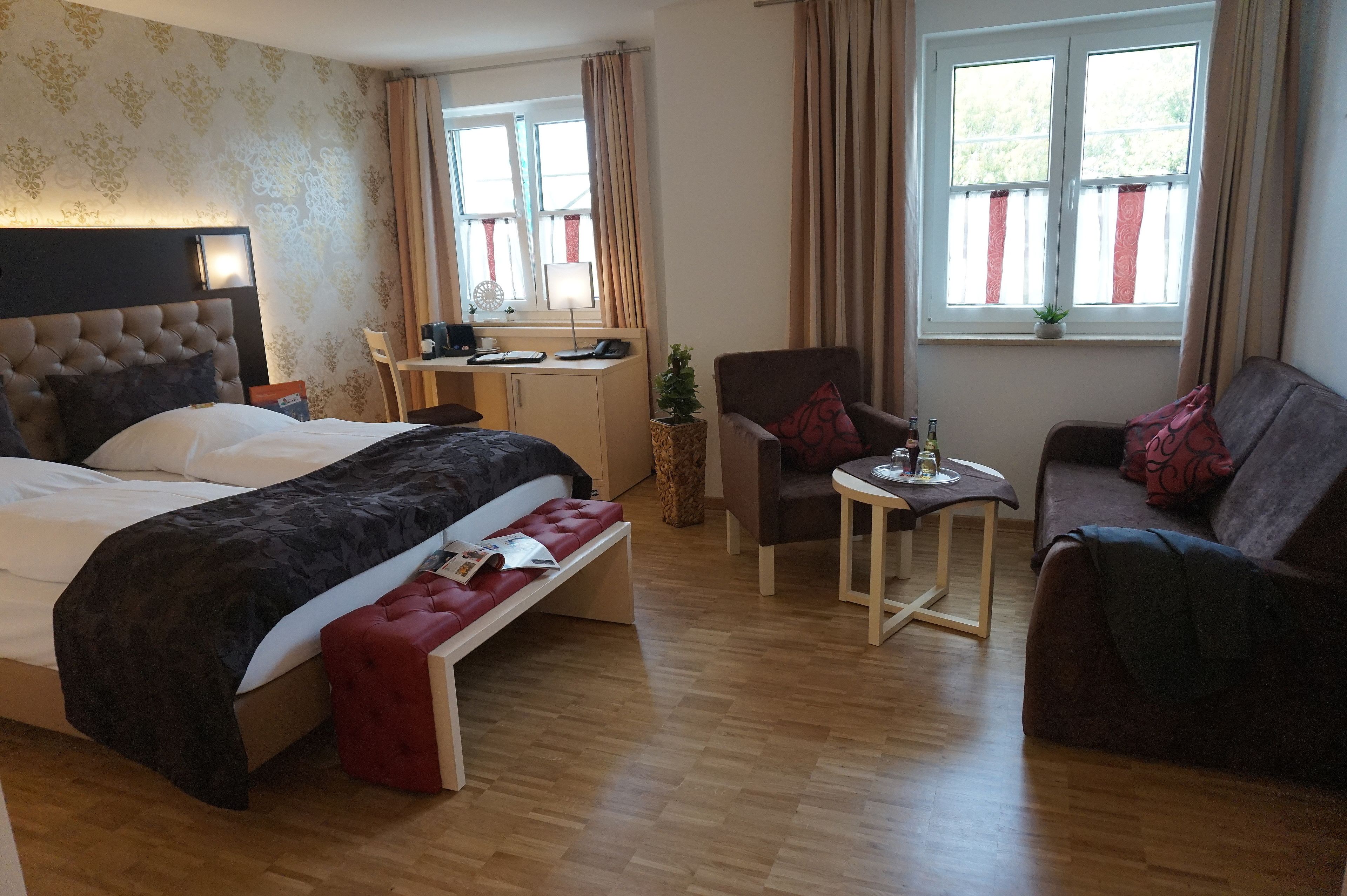 Une chambre d’hôtel avec un lit, un bureau, une chaise, un canapé et une fenêtre avec des rideaux.