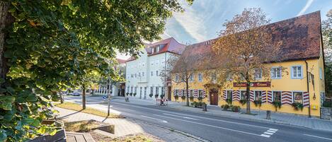 A street view with a yellow building, a bench, and a tree.